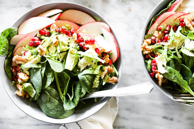 Horizontal image of apple walnut spinach salad in two bowls with forks dug in. 