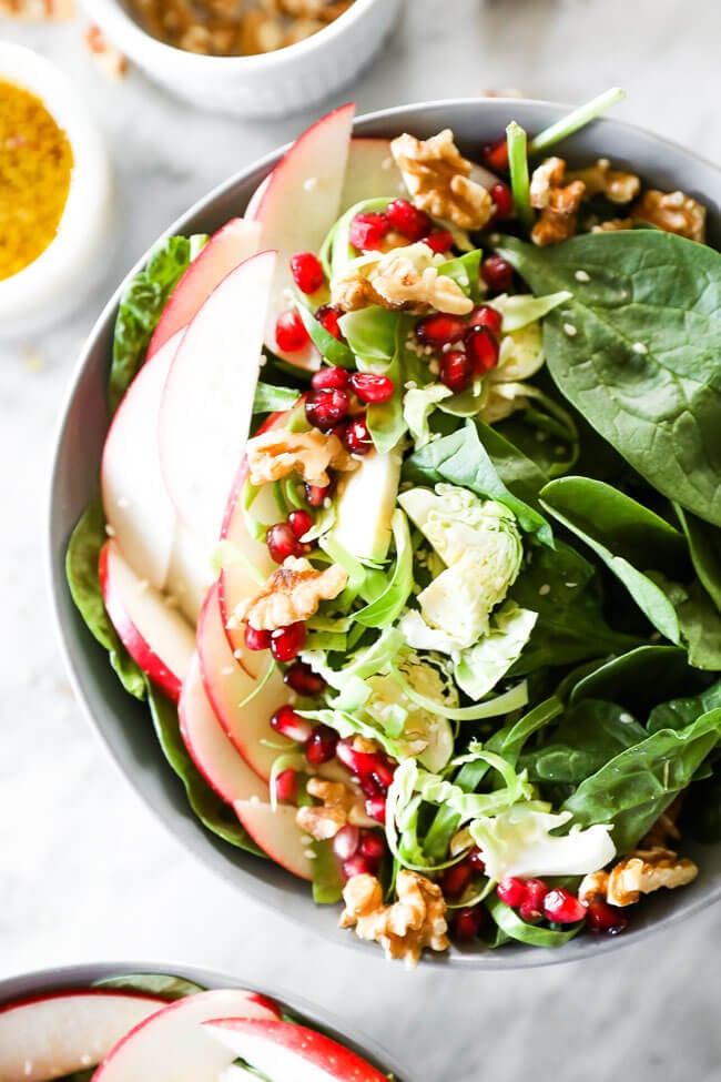 Close up vertical image of apple walnut spinach salad in a bowl. 