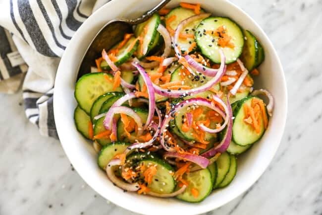 Asian cucumber salad in a bowl with spoon. Red onion and sesame seeds on top