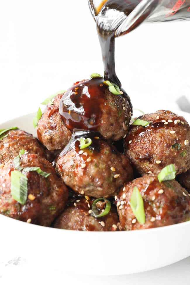 Vertical angled shot of pouring sauce over a bowl of asian meatballs. 