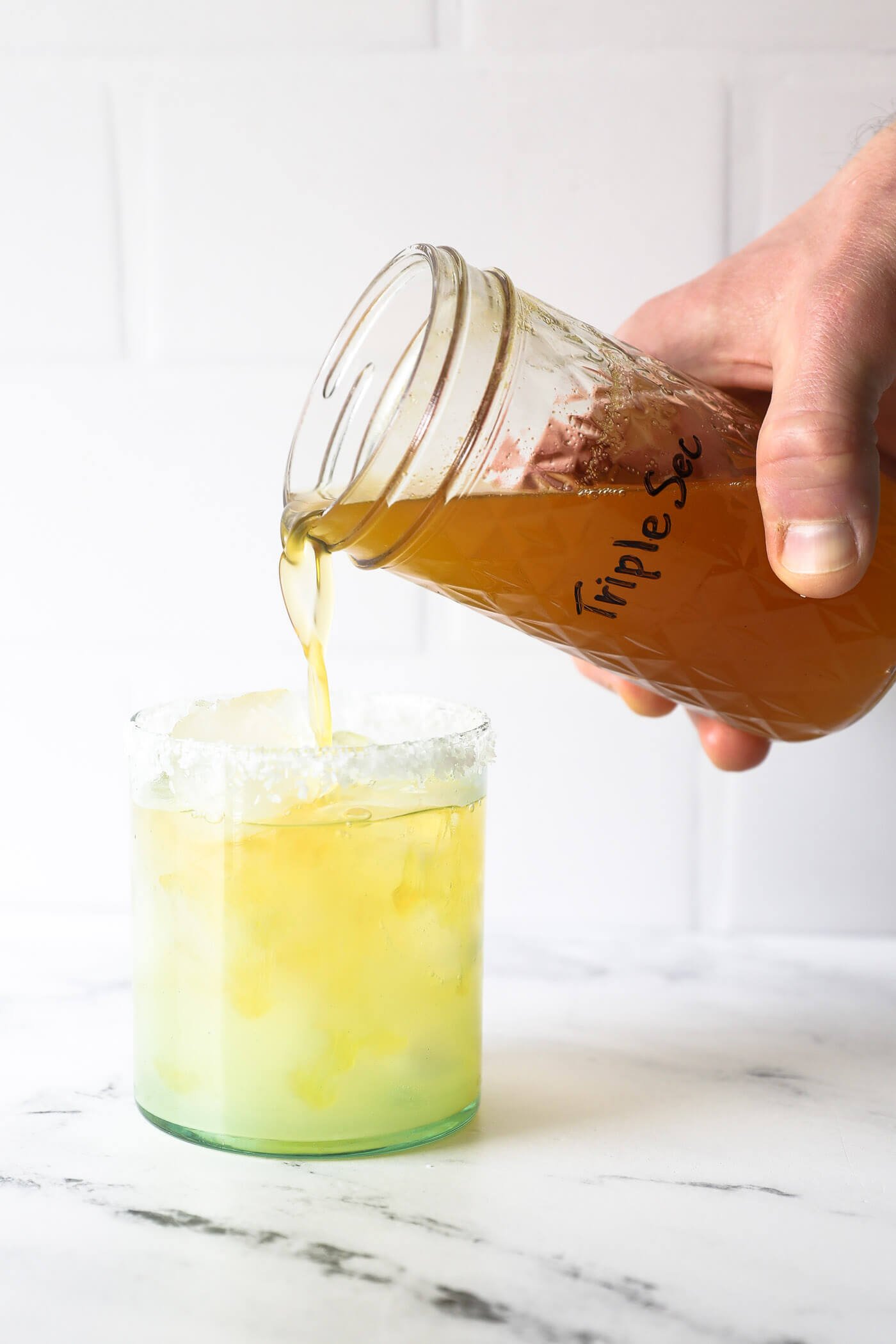 Hand pouring homemade triple sec into a margarita