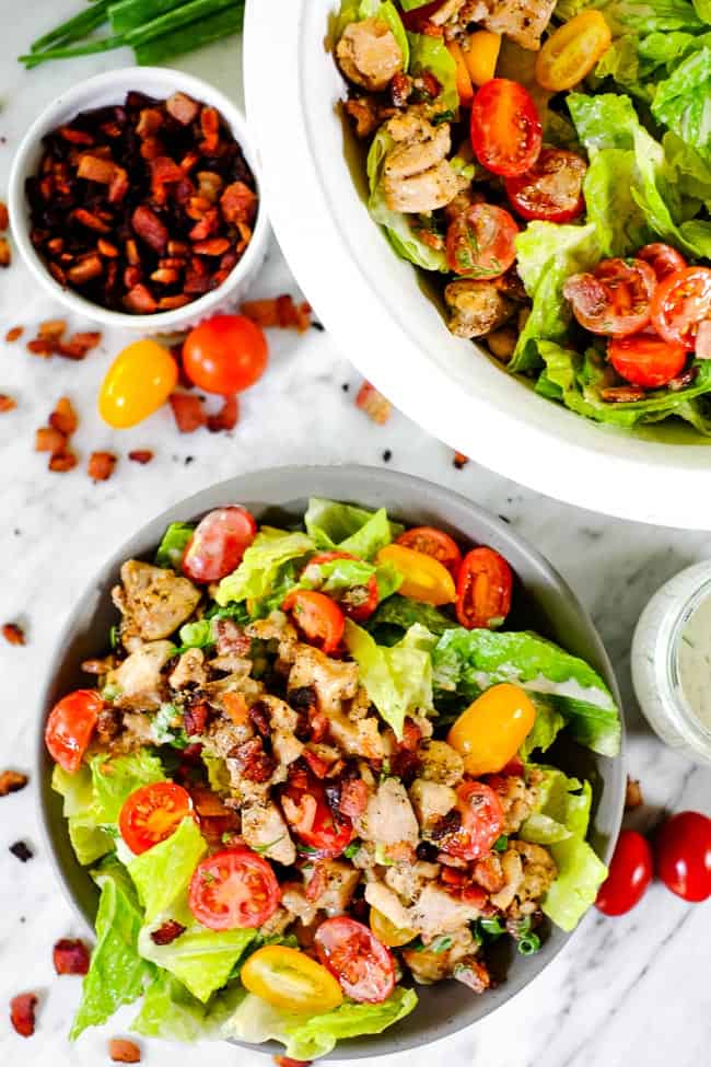 BLT salad in a bowl with larger serving bowl, extra bacon, tomatoes and dressing on the side. 