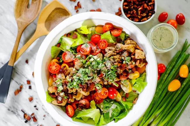 BLT salad in a large bowl with green onion, bacon, dressing and utensils. 