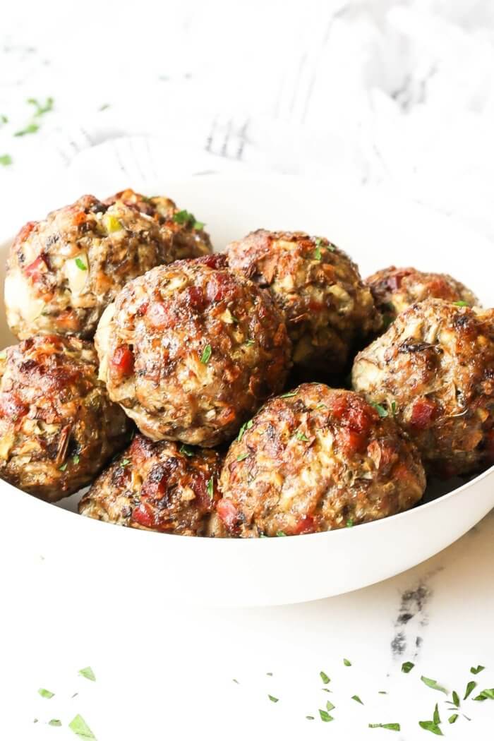 Angled image of a breakfast sausage meatballs piled up in a bowl. Fresh parsley sprinkled on top.