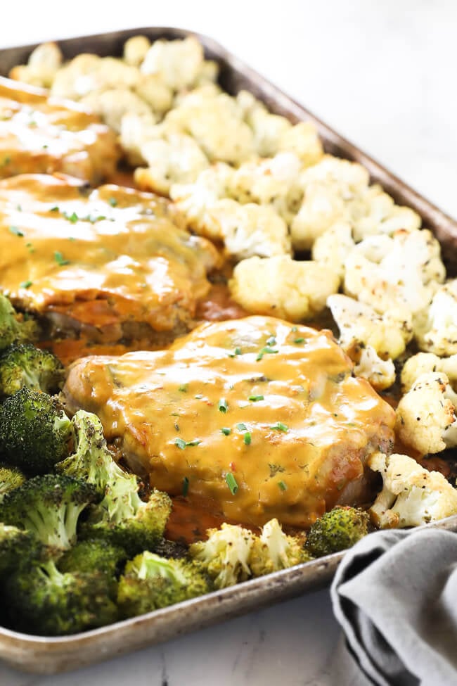 Angled image of honey mustard pork chops on a sheet pan with broccoli and cauliflower. 