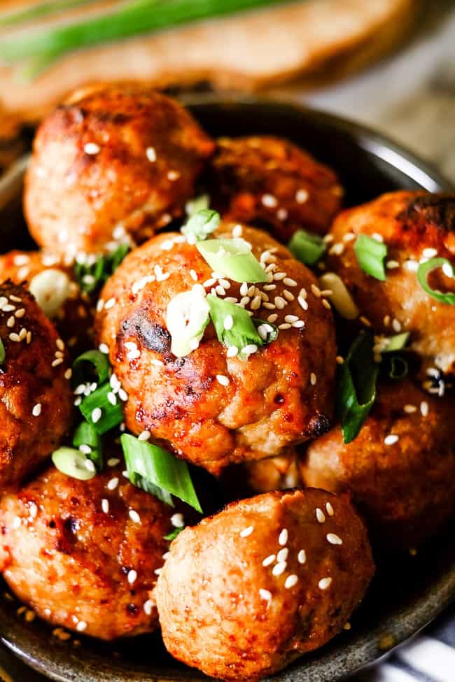 Close up shot of baked turkey meatballs in bowl with chopped green onion and sesame seeds on top. 