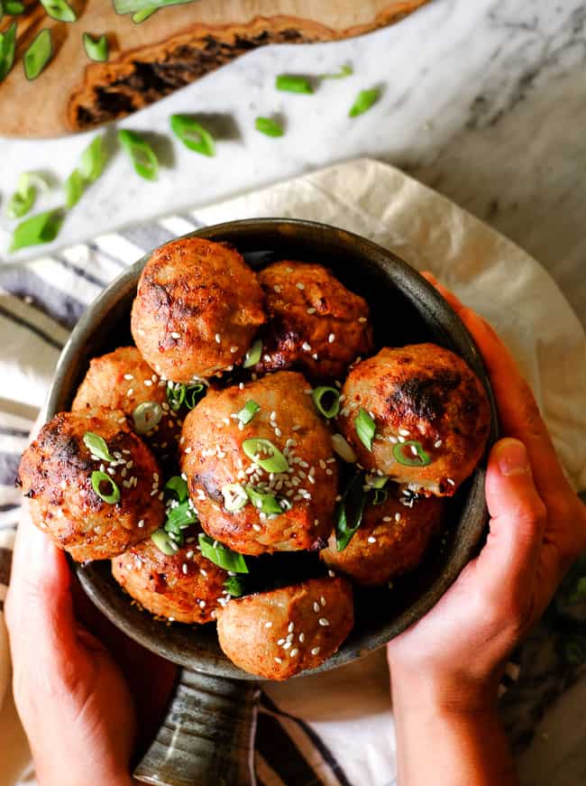 Baked turkey meatballs in a bowl with chopped green onion and sesame seeds on top. 