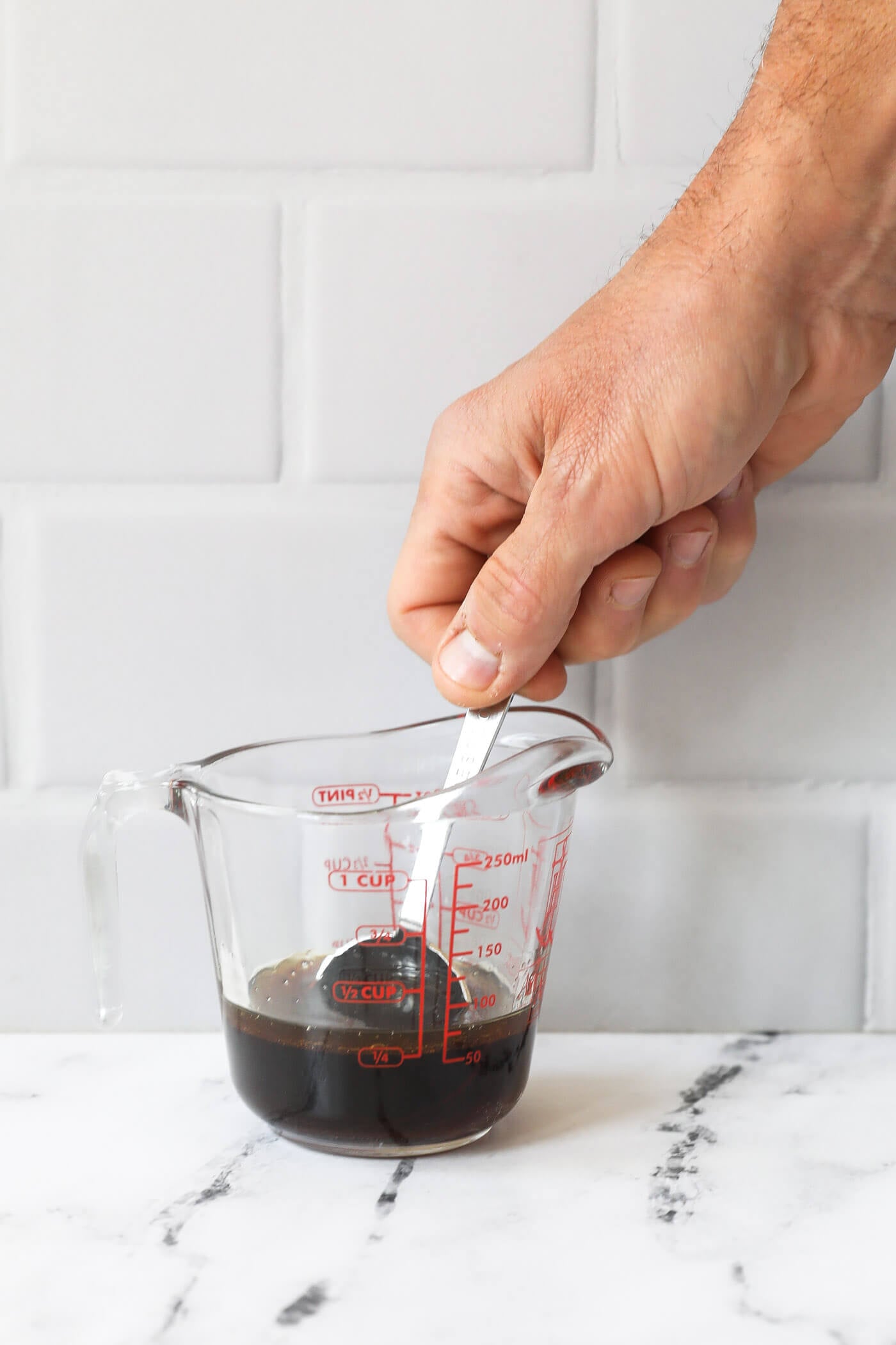 A hand mixing sauce up in mixing jar with a tablespoon.