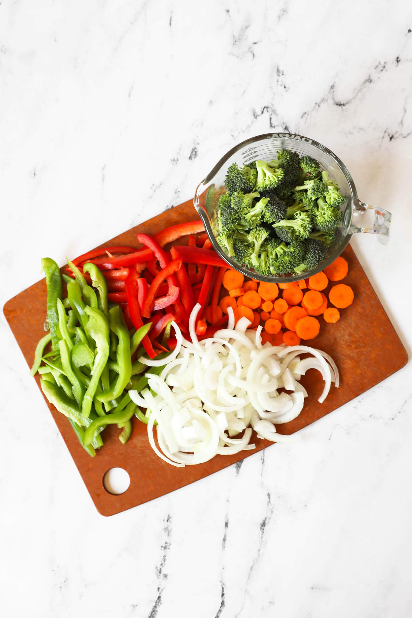 Chopped green and red bell pepper, onion, carrots and broccoli florets on a cutting board.