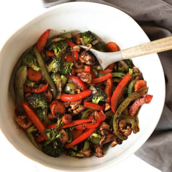 An overhead image of chicken stir fry in a large serving bowl with a serving spoon.
