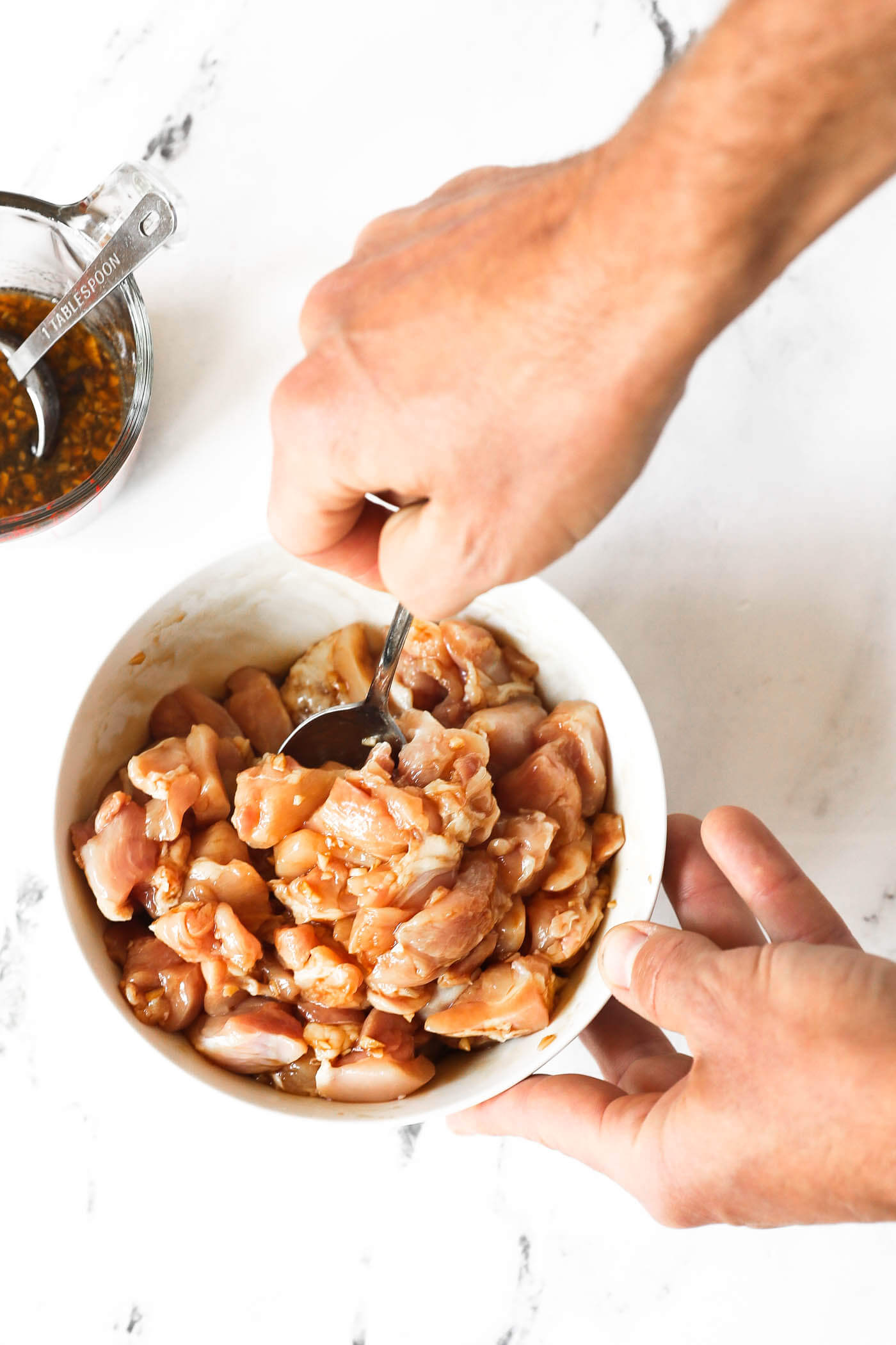 A person is holding a bowl of raw chicken pieces and mixing in a sauce.