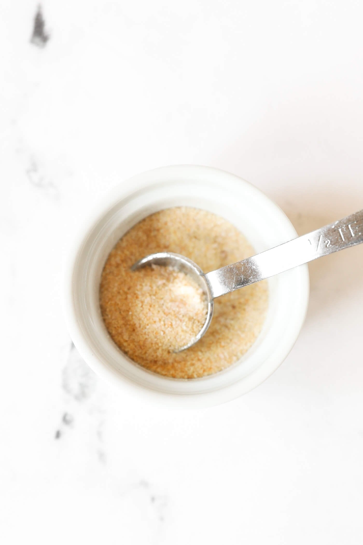 A small ramekin with seasonings and a measuring spoon.