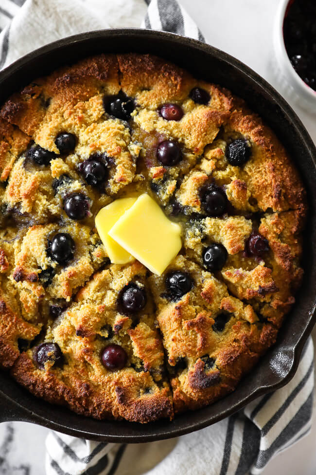 Vertical overhead close up image of blueberry cornbread in skillet with melting butter on top. 