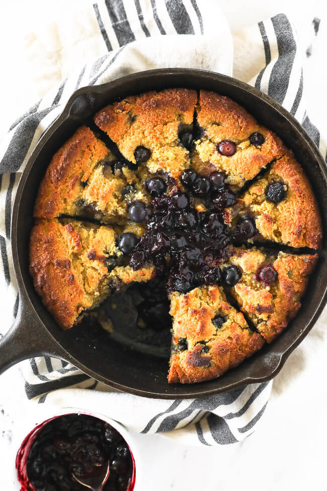 Vertical overhead image of gluten free and paleo cornbread in a skillet with blueberry sauce on top. 