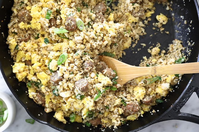 Breakfast fried rice in a skillet with a wooden spoon scooping some. 