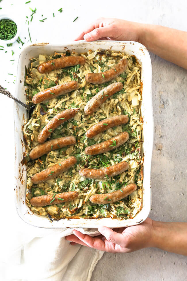 Vertical overhead image of placing the dish on the table. Baking dish filled with breakfast hashbrown casserole and sausages. 