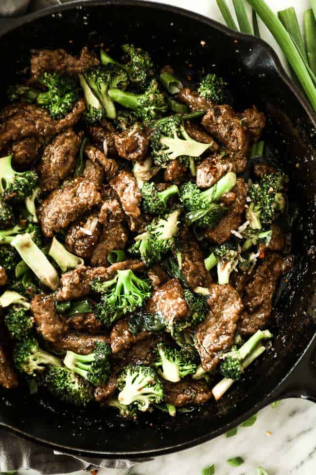 Broccoli beef stir fry in a cast iron skillet. Strips of beef stir fried with broccoli florets and chopped green onion and an asian inspired sauce. 