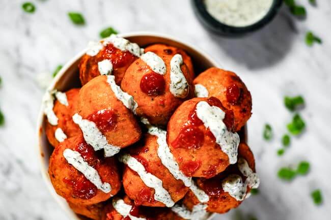 Buffalo chicken meatballs in a bowl with ranch and hot sauce drizzled on top. Garnished with chopped green onion. 