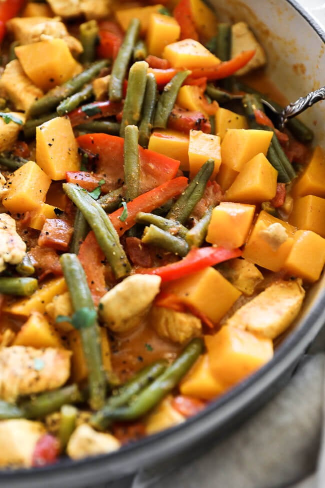 Angled vertical image of butternut squash curry in a skillet with a serving spoon. 