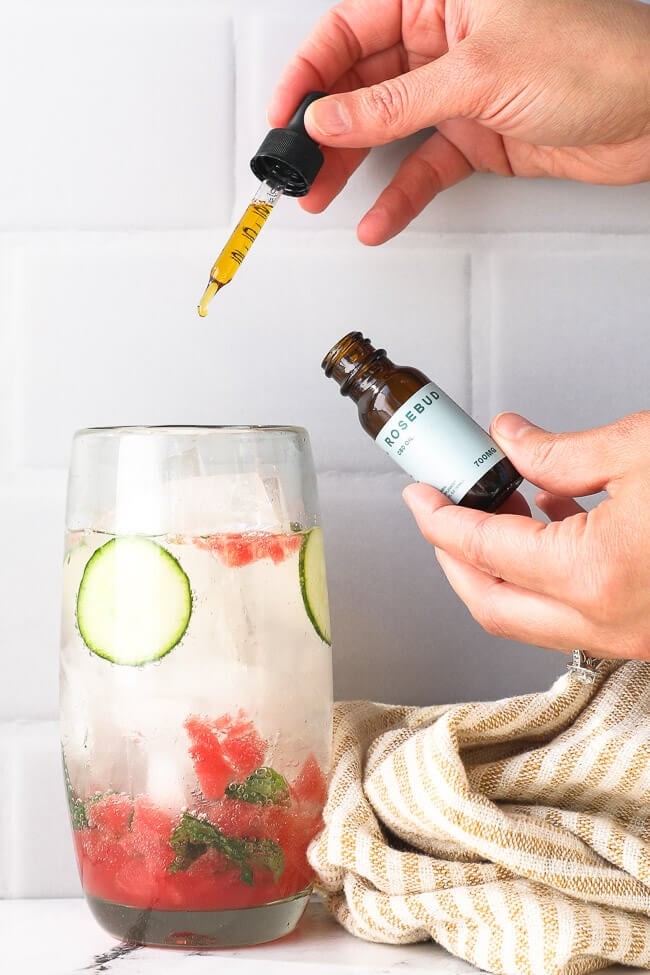 Image of using a dropper of Rosebud CBD to add CBD to a watermelon cucumber mojito mocktail. 