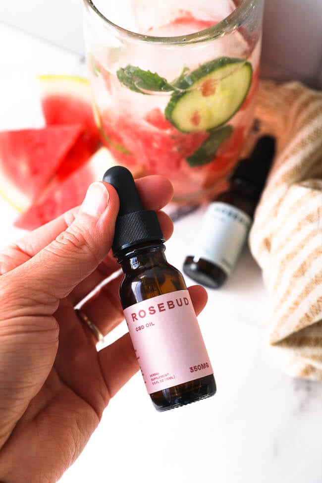 Holding a bottle of CBD oil with watermelon mojito mocktail in the background. 