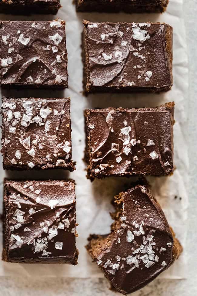 six chocolate tahini brownies with sea salt sprinkled on top. One brownie with a bite out.