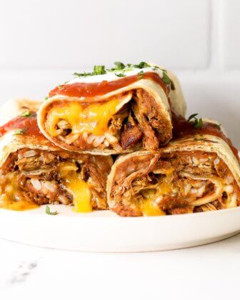 Straight on shot of 3 baked carnitas burritos on a plate with salsa and sour cream on top