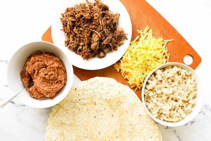 Overhead shot of burrito tortilla, refried beans, carnitas, cheese and rice