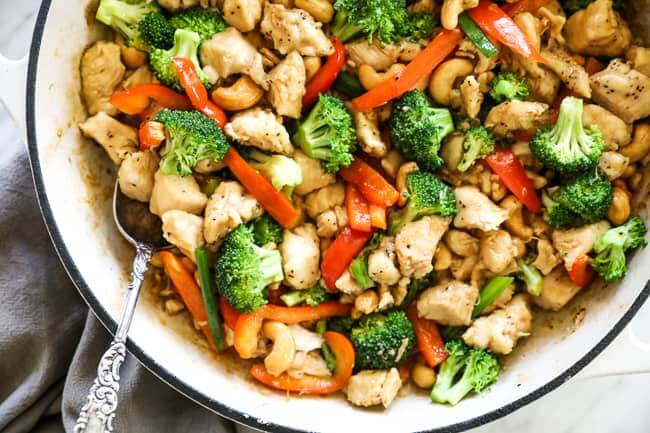 Overhead image of cashew chicken in a skillet with a serving spoon dipped in. Chicken, cashews, broccoli, red bell pepper and an asian sauce. 