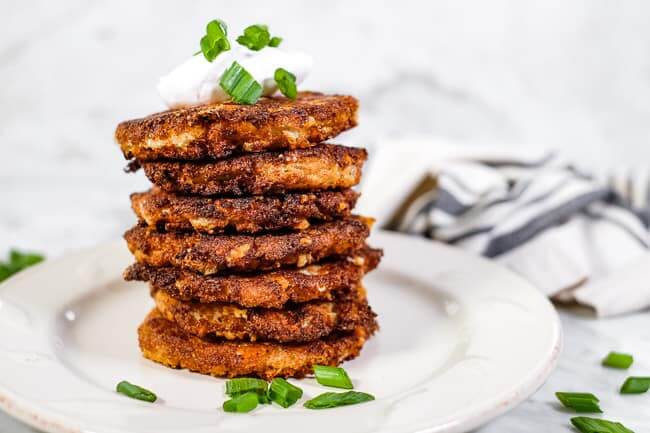 Stack of cauliflower fritters, topped with coconut yogurt and chopped green onion. 