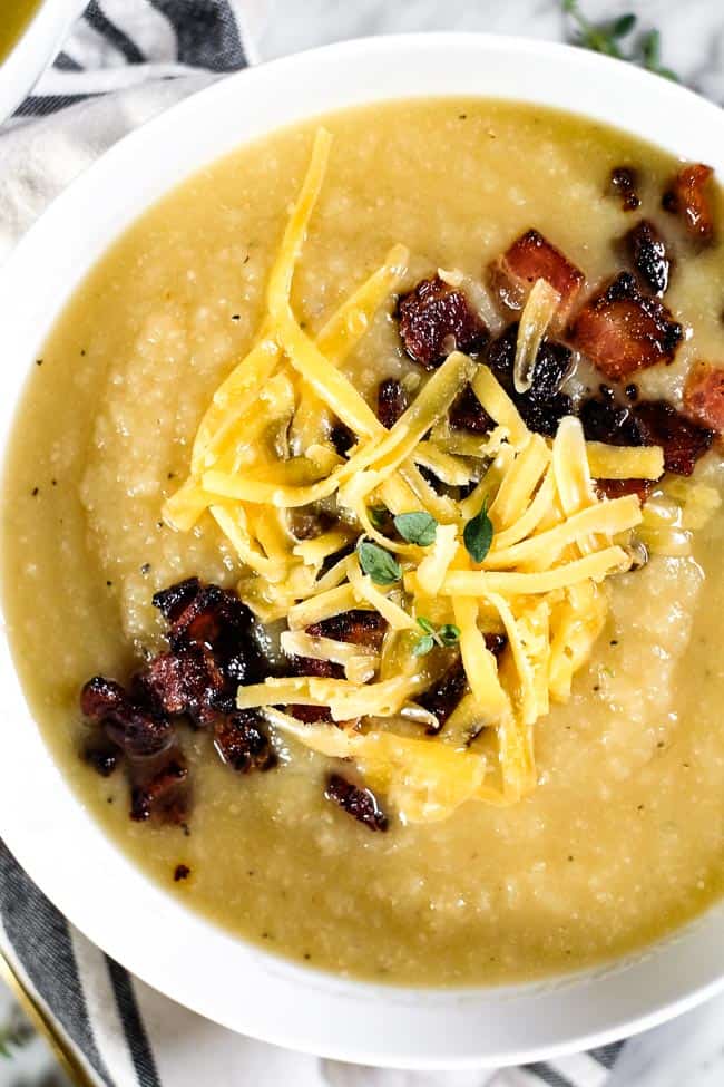 Celeriac soup in a bowl topped with bacon, shredded cheese and fresh thyme. 