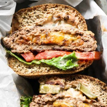 Close up overhead image of cheese stuffed keto burgers in a basket with buns, lettuce and tomato