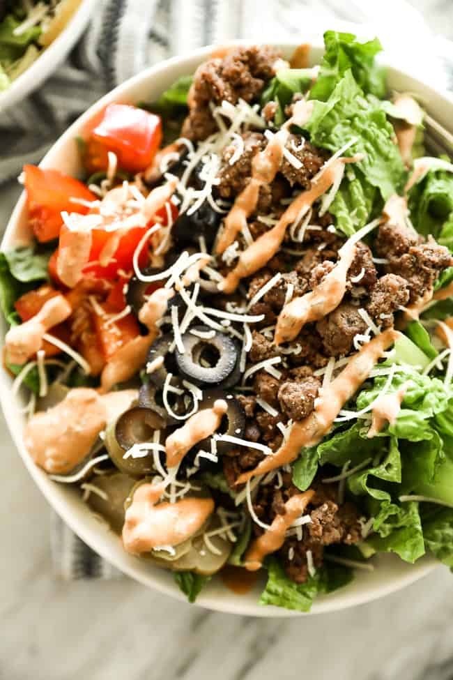 cheeseburger salad in a bowl with shredded cheese on top and special sauce drizzled over the top. 