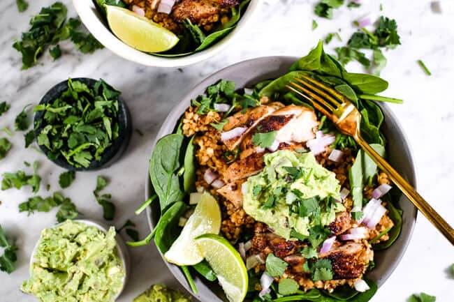 Chicken burrito bowl served up with a side of cilantro, guacamole and lime wedges. 