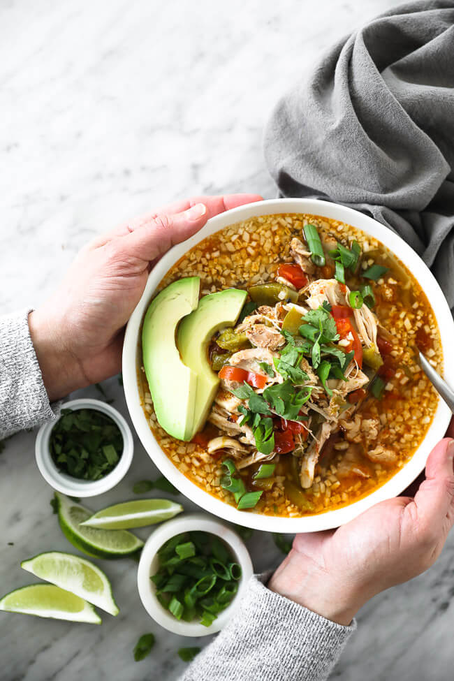 Holding a bowl of chicken fajita soup topped with chopped green onion, cilantro and sliced avocado. 