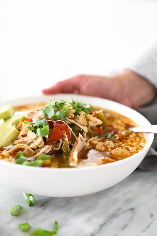 Angled shot of soup in a bowl with a hand in the background setting the bowl down on the table. 