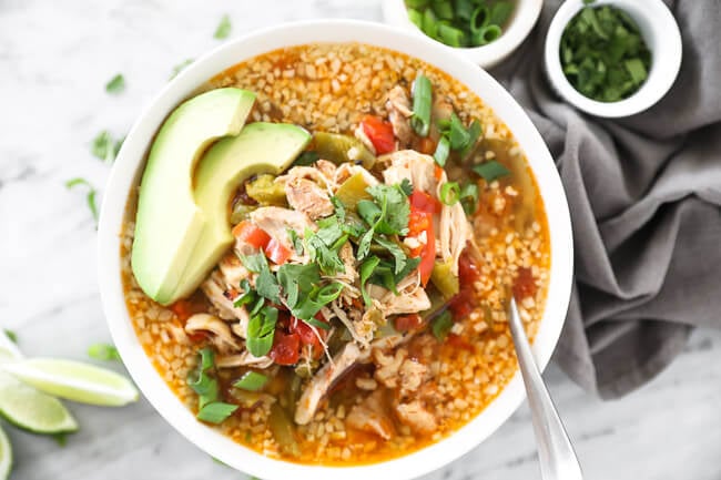 Bowl of chicken fajita soup with a spoon in it. Topped with chopped green onion, cilantro and sliced avocado. 
