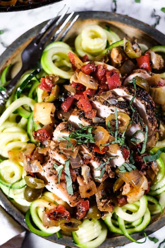 Close up shot of chicken in tomato sauce on a plate with zoodles and fresh basil on top. 