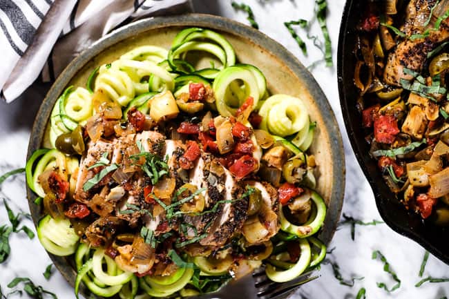 Chicken in tomato sauce served on a plate over zoodles with fresh basil on top. 