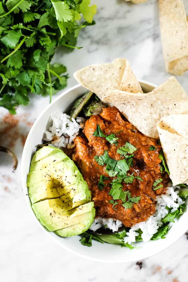 Chicken mole recipe in a bowl with greens, rice, avocado and grain free tortilla chips. Topped with chopped cilantro. 