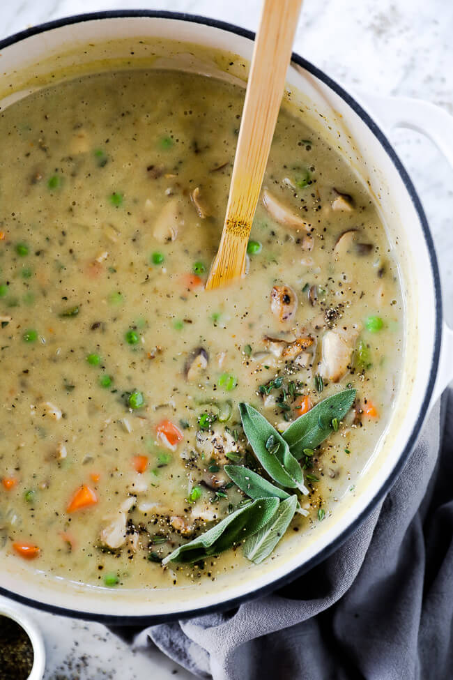 Close up vertical image of chicken pot pie soup in dutch oven with wooden spoon. Garnished with fresh sage, thyme and ground pepper. 