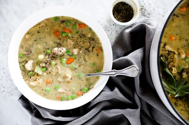 Horizontal image of chicken pot pie soup served in a bowl with a spoon and extra pepper sprinkled on top. 