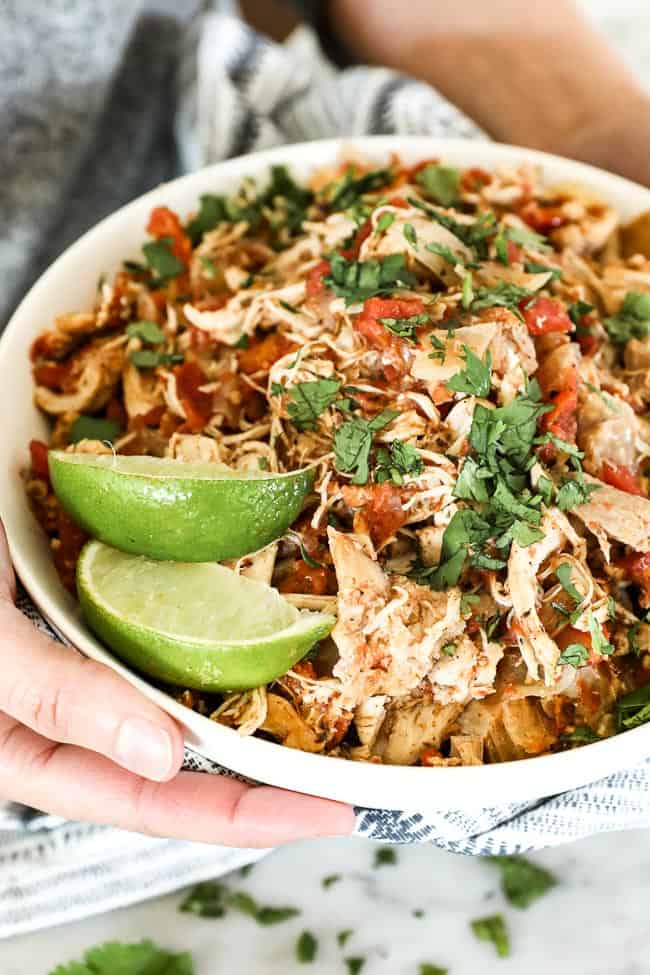 Holding a bowl of shredded chicken with cilantro and lime wedges. 