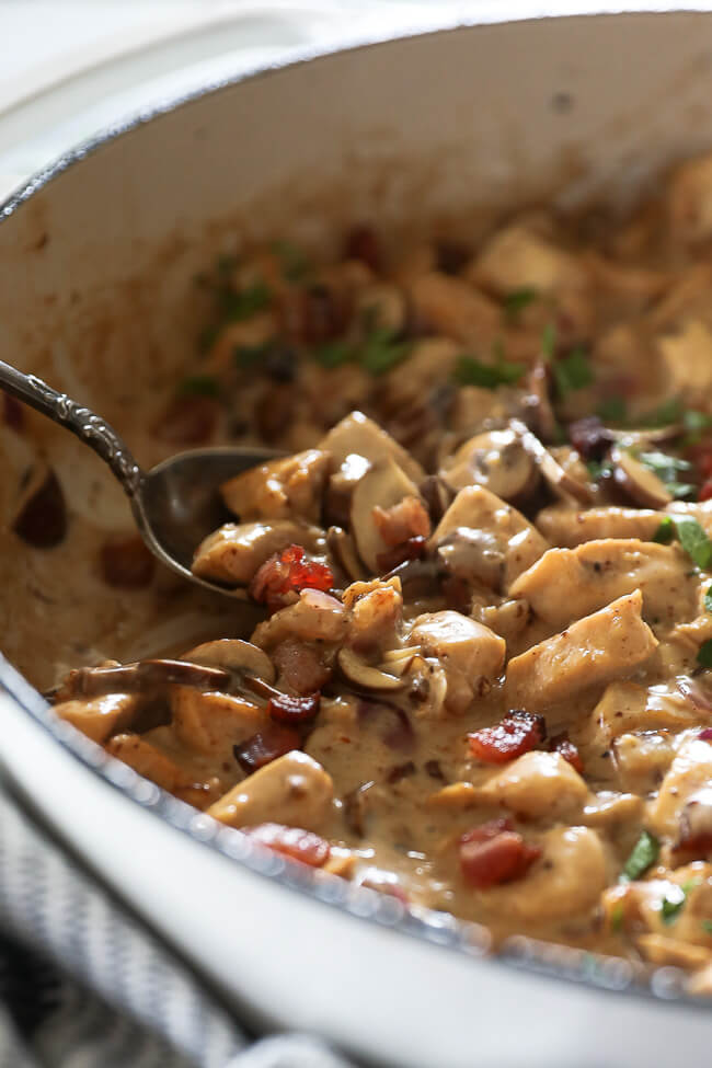 Angled shot of chicken with creamy mushroom sauce in a skillet with a serving spoon scooping some up. 