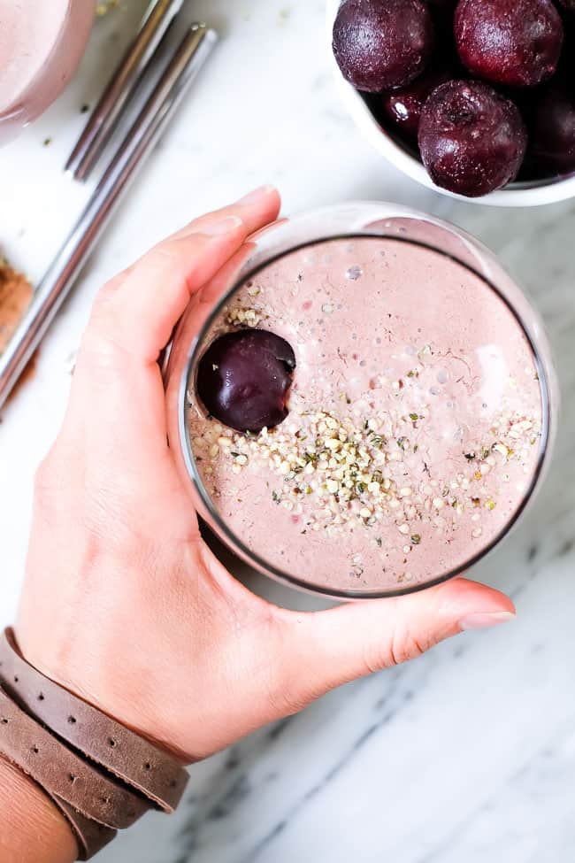 Holding chocolate cherry smoothie in glass with hempseed and cherry topping. 