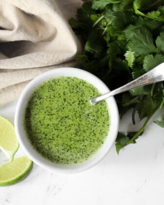 Overhead shot of fresh cilantro lime sauce in a ramekin with a spoon coming out and fresh cilantro and lime wedges