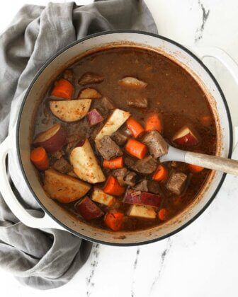 Overhead shot of dutch oven beef stew with potatoes and carrots and spoon sticking out