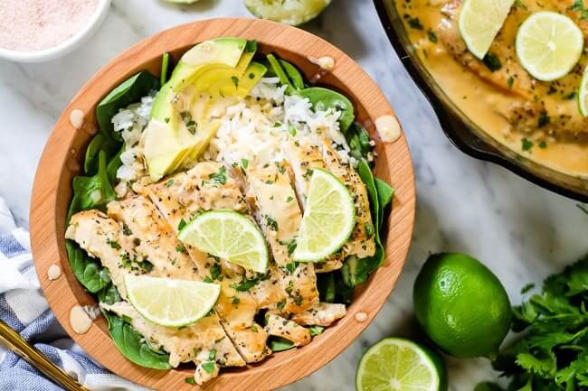 This Paleo and Whole30 friendly coconut lime chicken is so flavorful, fresh and satisfying! Coconut lime chicken in a bowl with spinach, rice, avocado and lime wedges and cilantro on top.