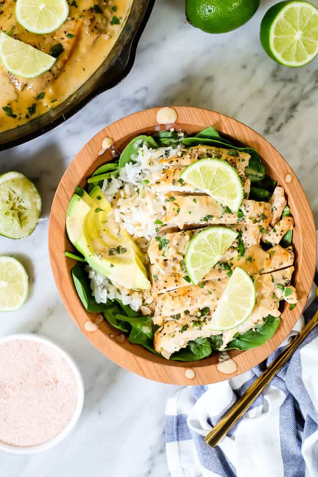 This Paleo and Whole30 friendly coconut lime chicken is so flavorful, fresh and satisfying! Coconut lime chicken in a bowl with spinach, rice, avocado and lime wedges and cilantro on top.
