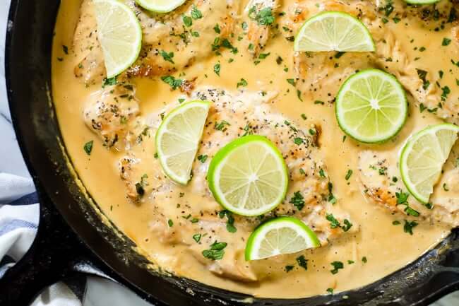 This Paleo and Whole30 friendly coconut lime chicken is so flavorful, fresh and satisfying! Coconut lime chicken in cast iron skillet with lime wedges and cilantro on top.